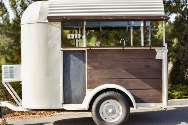Cream colored horse trailer converted to mobile bar equipped with four keg taps