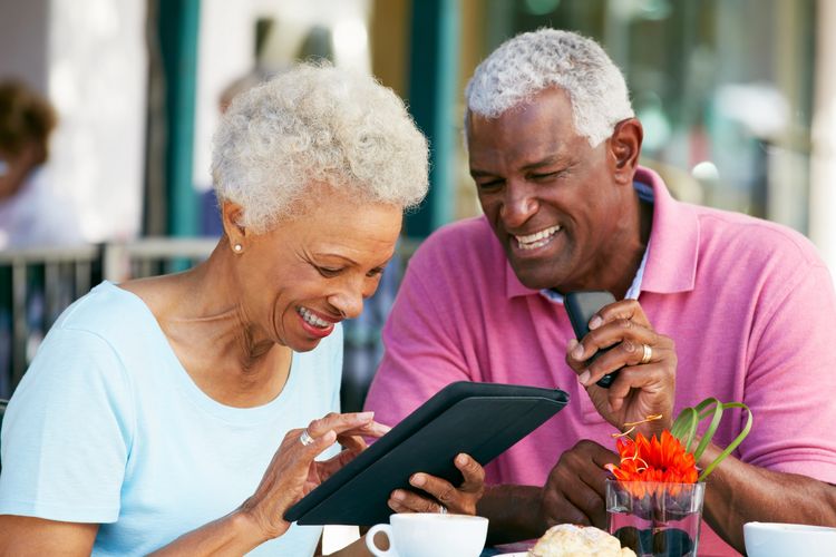 Smiling elderly couple using a tablet at a café.