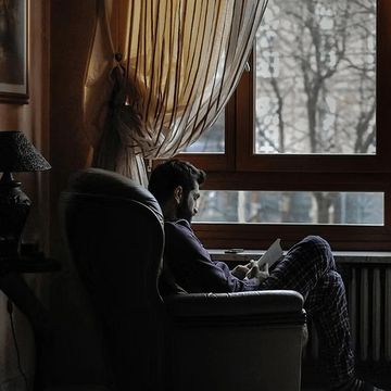 Man reading by a window in a cozy room with soft lighting.