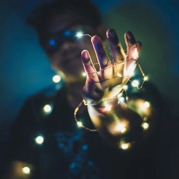 Person holding glowing fairy lights in a dark setting.