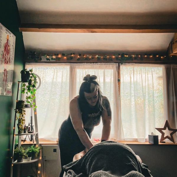 A woman giving a massage in a cozy, softly lit room with plants and star decorations.