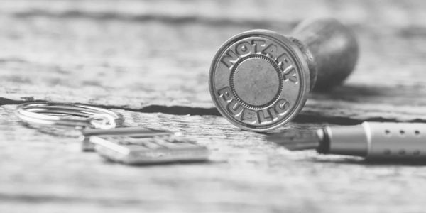 Close-up of a notary public stamp on a wooden surface with a pen and keychain nearby.