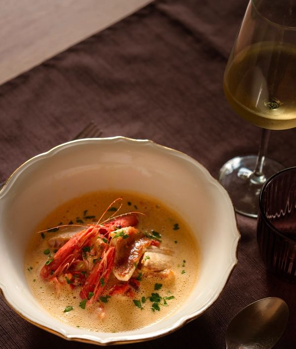 A bowl of seafood soup with prawns and herbs, paired with a glass of white wine.