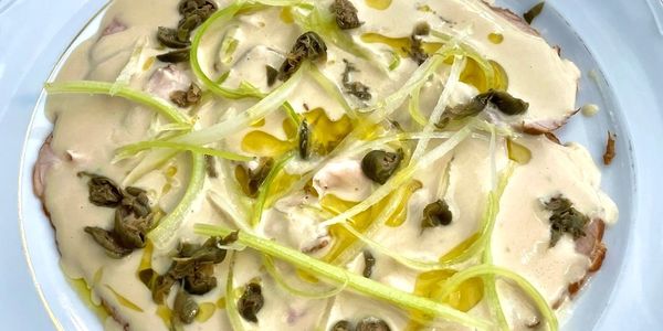 Thinly sliced meat with creamy sauce, capers, and green garnish.