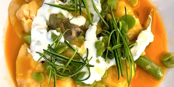 Close-up of ravioli pasta with green vegetables and creamy sauce.