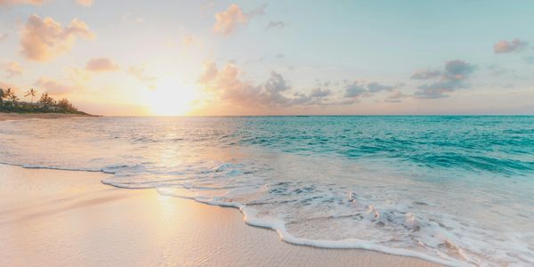 Sunset over a tranquil beach with gentle waves and soft sand.