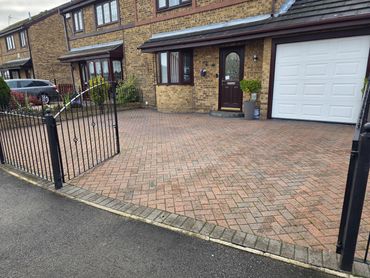 Brick-paved driveway with open black metal gate and brick house.