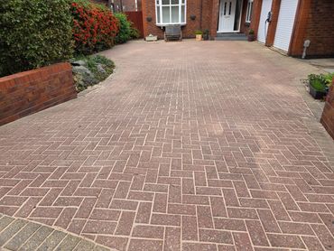 A clean brick-paved driveway in front of a brick house with greenery.