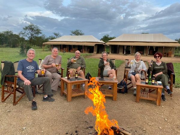 A group of people enjoying drinks by the fire a luxury tented camp Serengeti