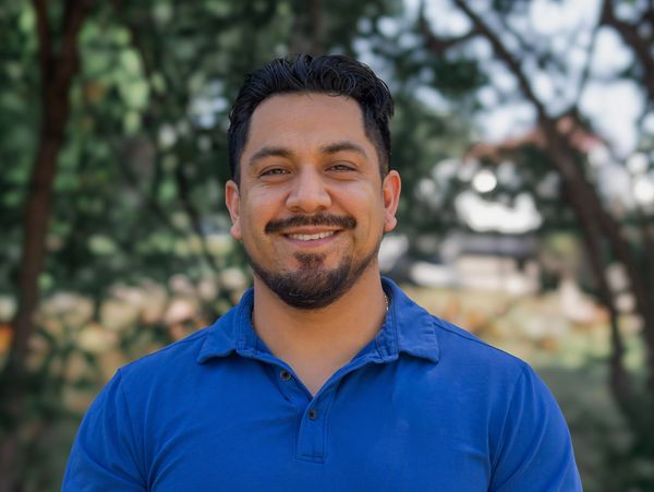 Man smiling outdoors in a blue shirt.