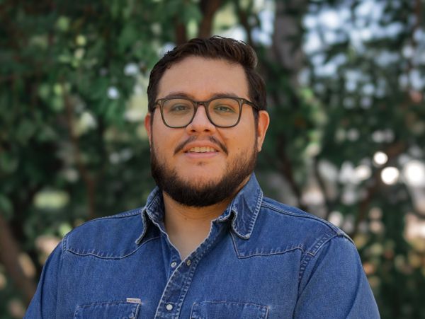Man with glasses wearing a denim shirt outdoors.
