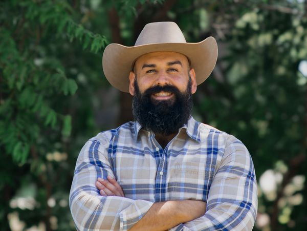 Smiling man in a plaid shirt and cowboy hat outdoors.