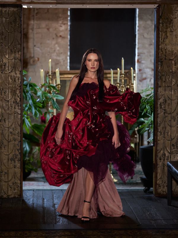A model in a striking red and beige gown walking indoors.