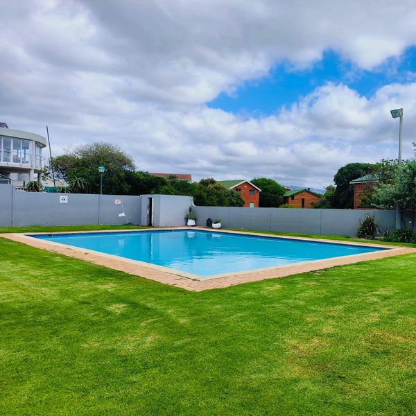 A clean swimming pool surrounded by green grass under a partly cloudy sky.