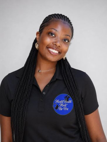 Smiling woman with long braids in a black polo shirt.