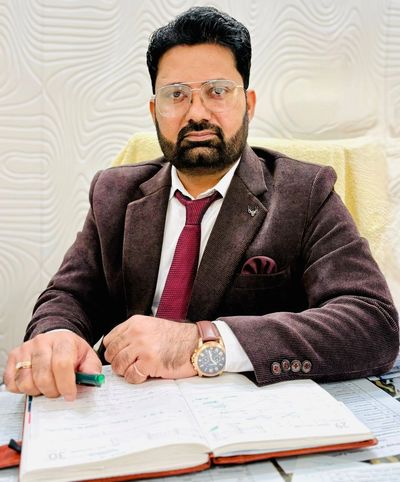 A serious man in a suit sitting at a desk with an open book.