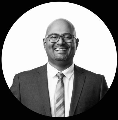 Smiling man in a suit and tie with glasses against a white background.