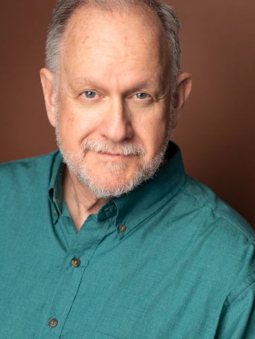Smiling middle-aged man in teal shirt against brown background.