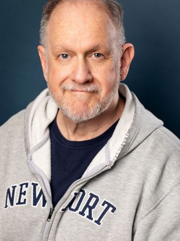Smiling man in a gray Newport hoodie against a dark background.
