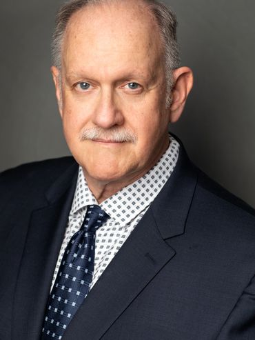 Professional headshot of a middle-aged man in a suit and patterned tie.