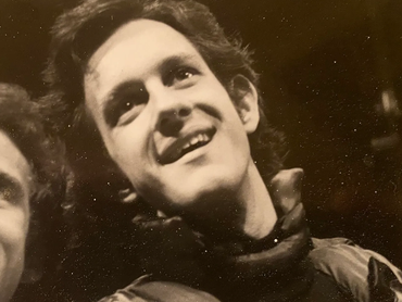 Black and white close-up of a smiling young man with curly hair.