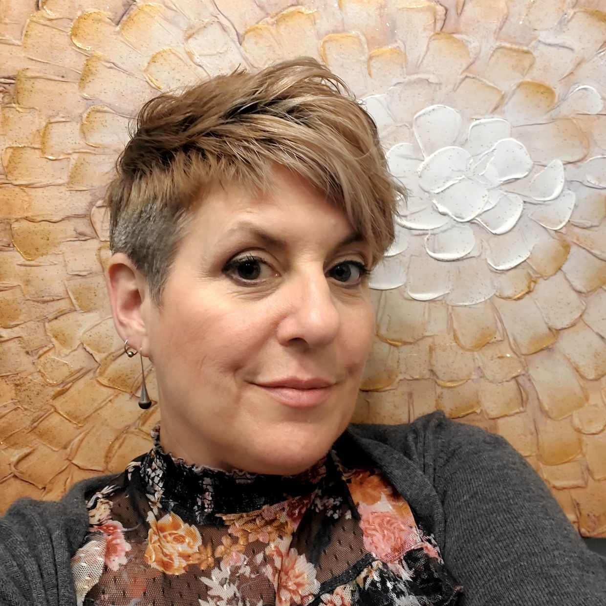 Smiling woman with short hair in front of a floral textured background.