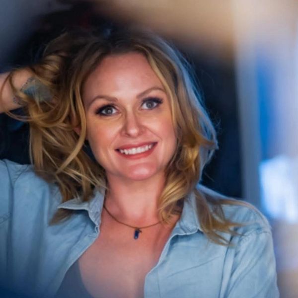 Smiling woman with blonde hair touching her hair.