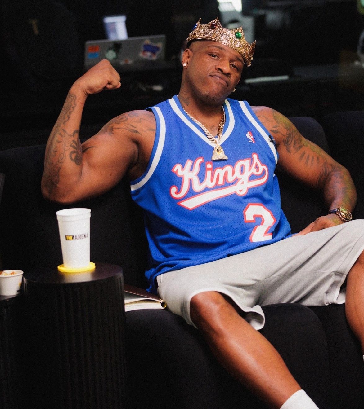 Man wearing a crown and Kings basketball jersey flexing on a couch.
