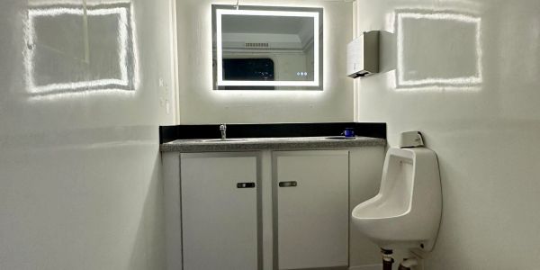 Modern bathroom with illuminated mirror and urinal.