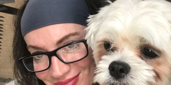 A woman with glasses and headband poses with her fluffy white dog.