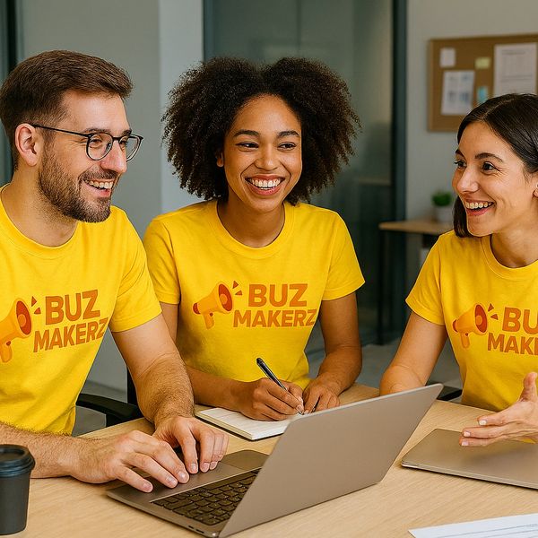 Three colleagues in matching yellow Buzz Makerz t-shirts collaborate happily around a laptop.