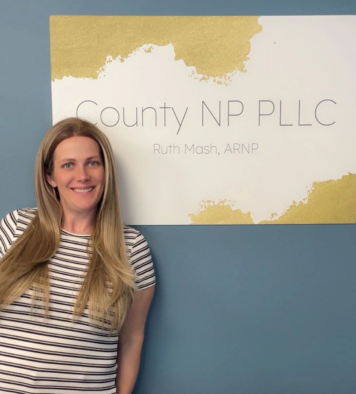 A smiling woman with long blonde hair stands by a sign for County NP PLLC.