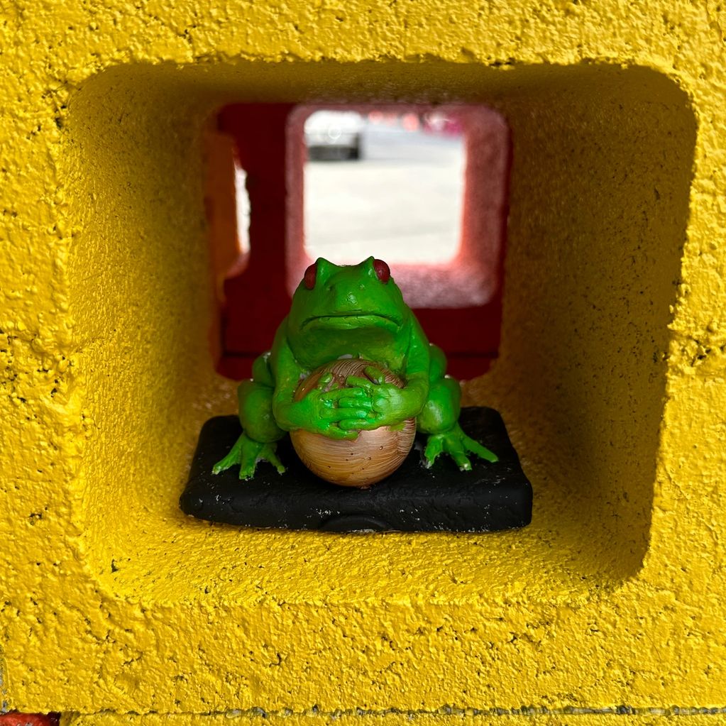 Green frog figurine holding a ball inside a yellow alcove.