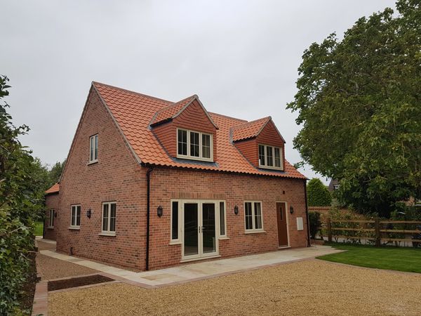 New build brick house with red tiled roof and beige window frames. Gravel driveway and turfed grass