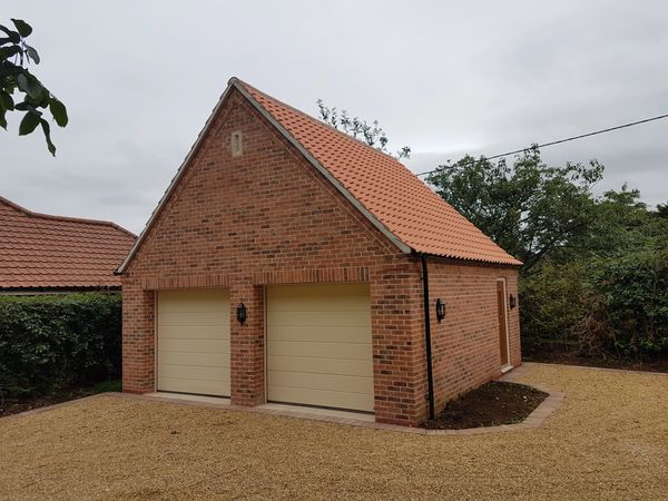 A brick double garage with beige doors and a tiled roof.