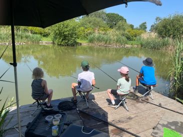 Four children fishing by a pond on a sunny day.