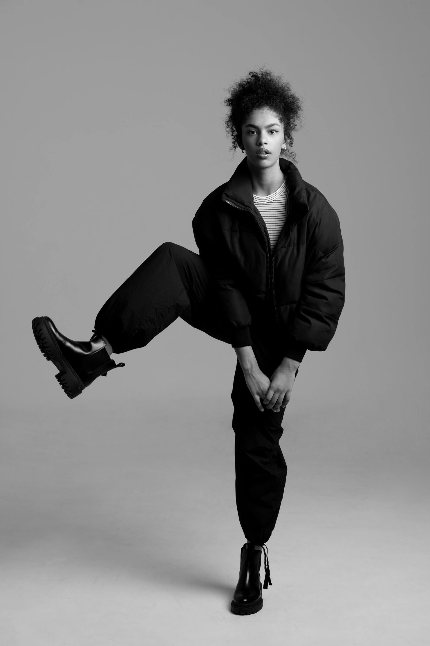 Young woman in black clothing striking a dynamic pose against a plain background.