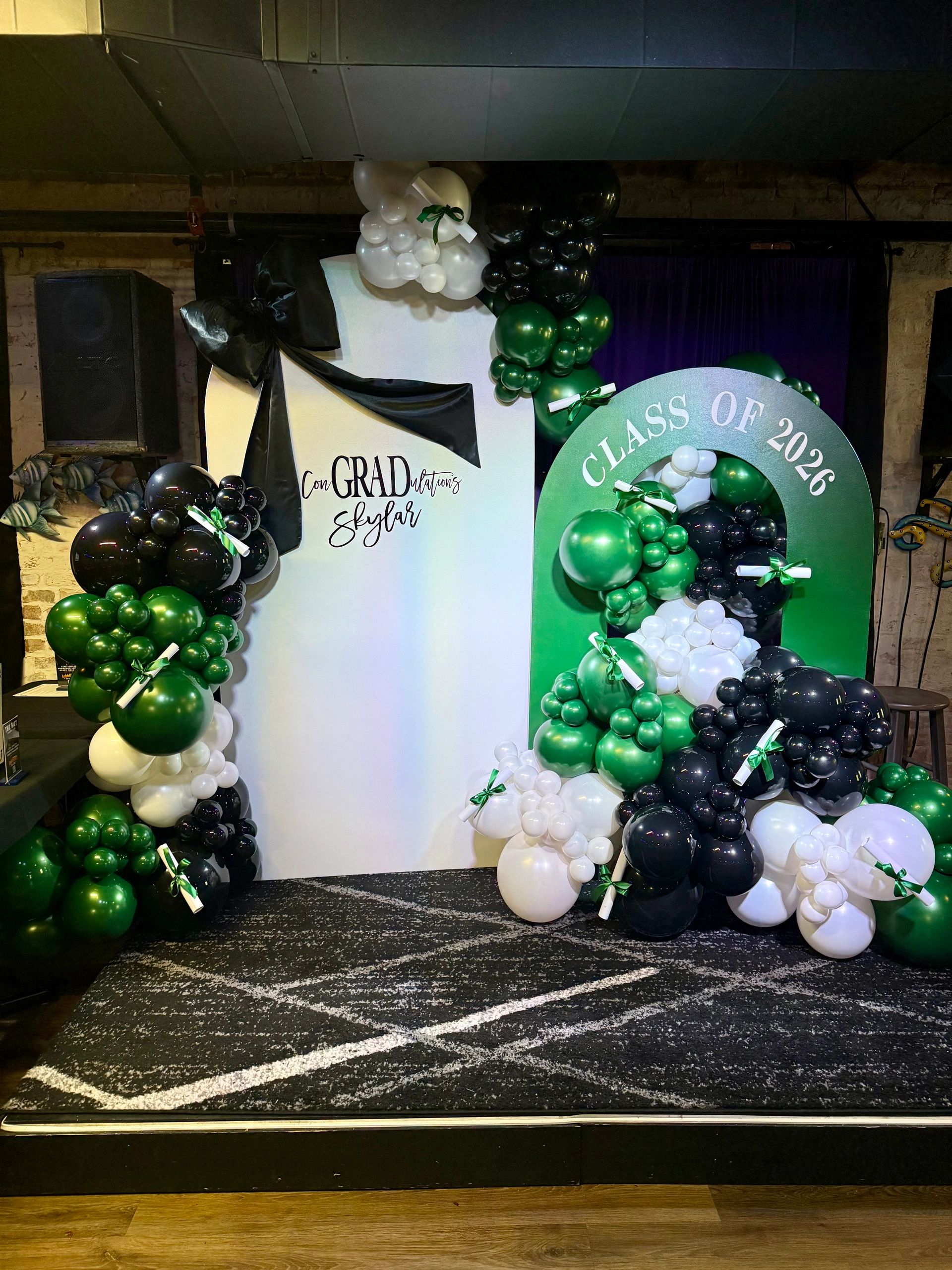 Graduation backdrop with green, black, and white balloons and a congratulatory message for Skylar.
