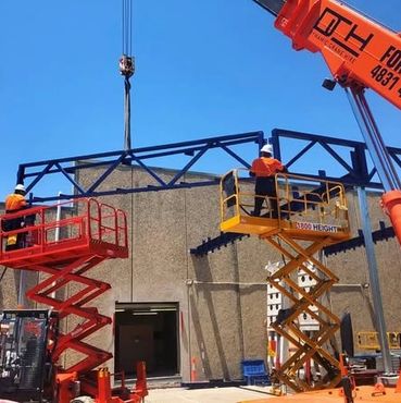 Workers using scissor lifts to install a steel beam on a building.