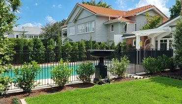 A suburban house with a fenced pool and green lawn under a blue sky.