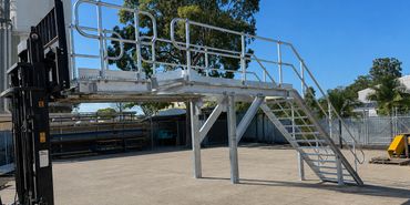 Metal platform with stairs supported by a forklift outdoors.
