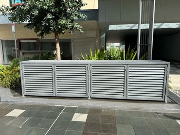 Modern outdoor utility box with louvered doors in an urban setting.