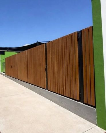 Long wooden fence panels with black metal supports along a concrete sidewalk.