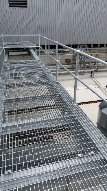 Metal walkway with safety railings on an industrial rooftop.