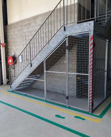 Metal staircase with a wire mesh enclosure underneath in an industrial setting.
