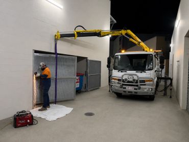 Worker using a grinder near a truck with a yellow crane at night.