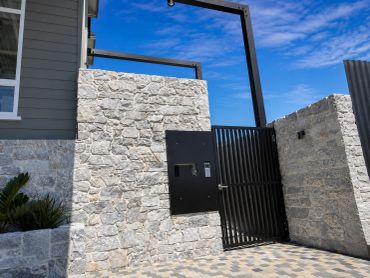 Modern stone wall with a metal gate under a bright blue sky.