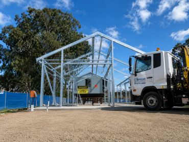 Construction of a steel frame structure with a truck nearby under a blue sky.