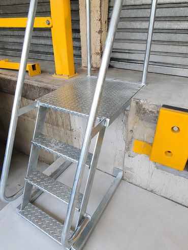 Metallic three-step ladder with handrails beside a concrete platform.