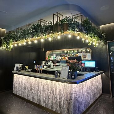 Modern bar with illuminated counter and overhead greenery.